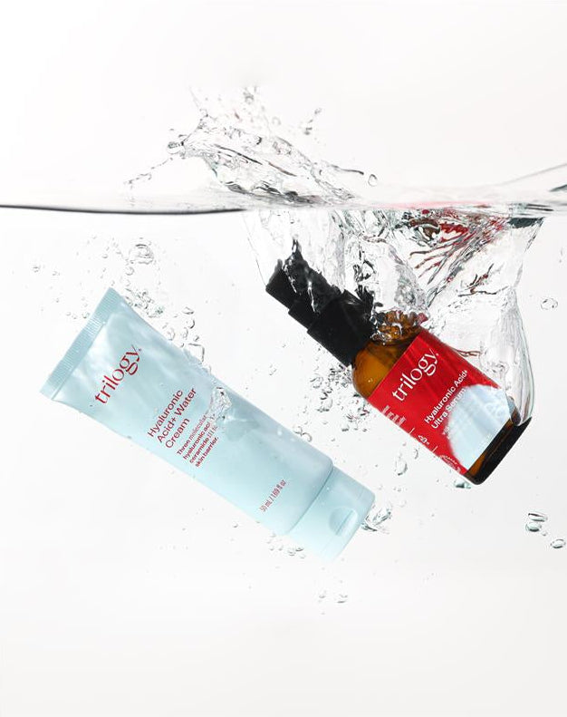 Two Trilogy skincare products splashing into water on a white background